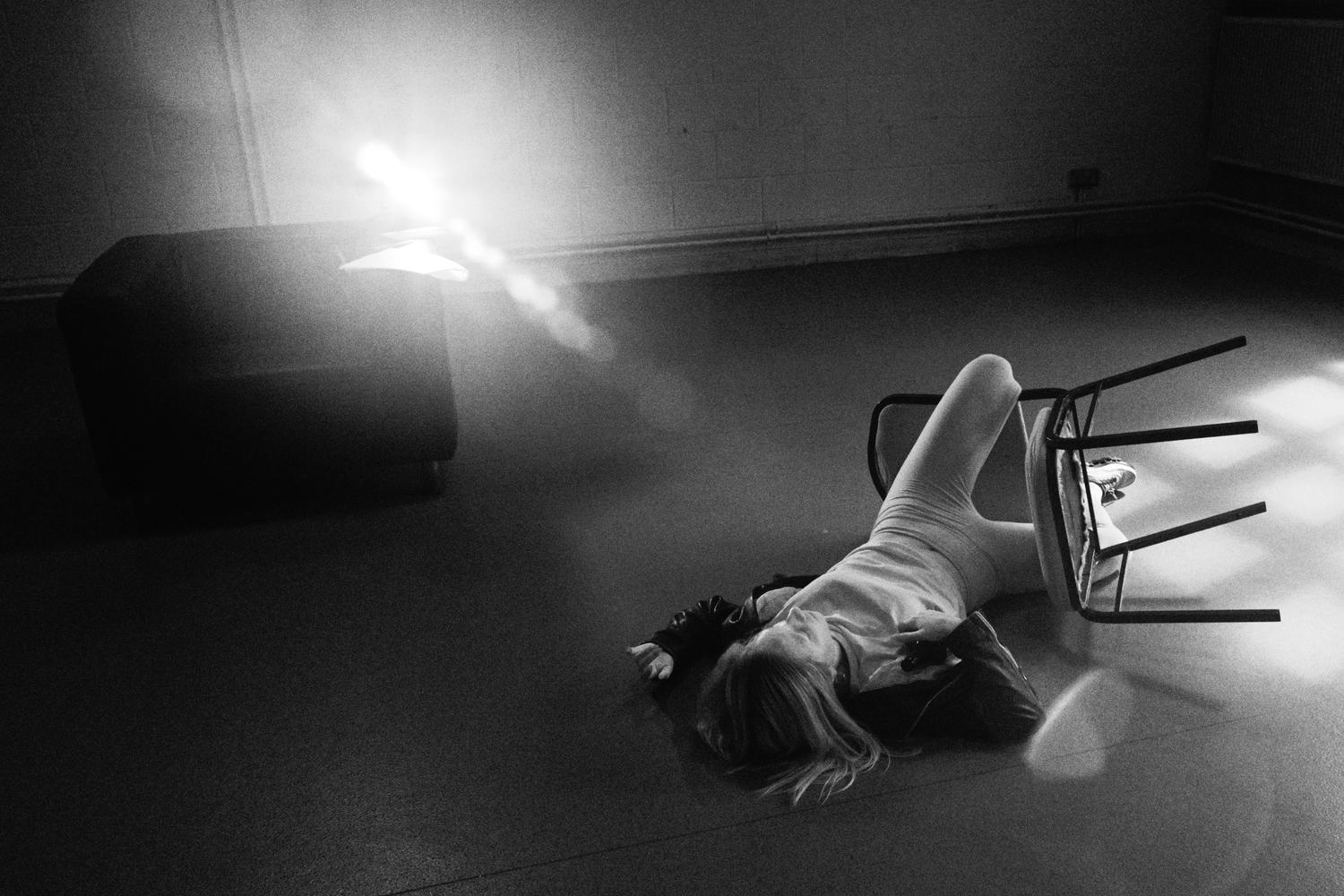 A figure lying on the floor beside an overturned chair in a shaft of light